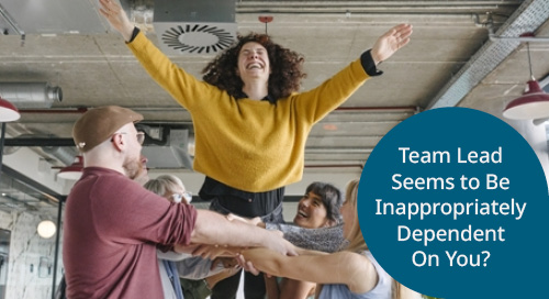 A group of diverse team members supporting a colleague standing on their hands in a bright, modern workspace, conveying teamwork and support.