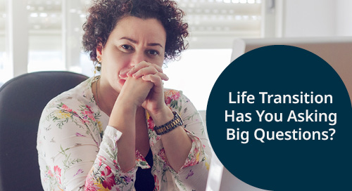 A woman with curly hair sits at a desk, looking thoughtfully with her hands clasped. She is wearing a floral blouse. A caption on the right reads, 'Life Transition Has You Asking Big Questions?'