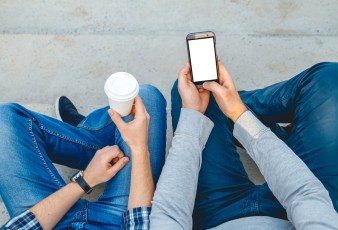 Two young men with the phone in his hand sitting on the steps. top view